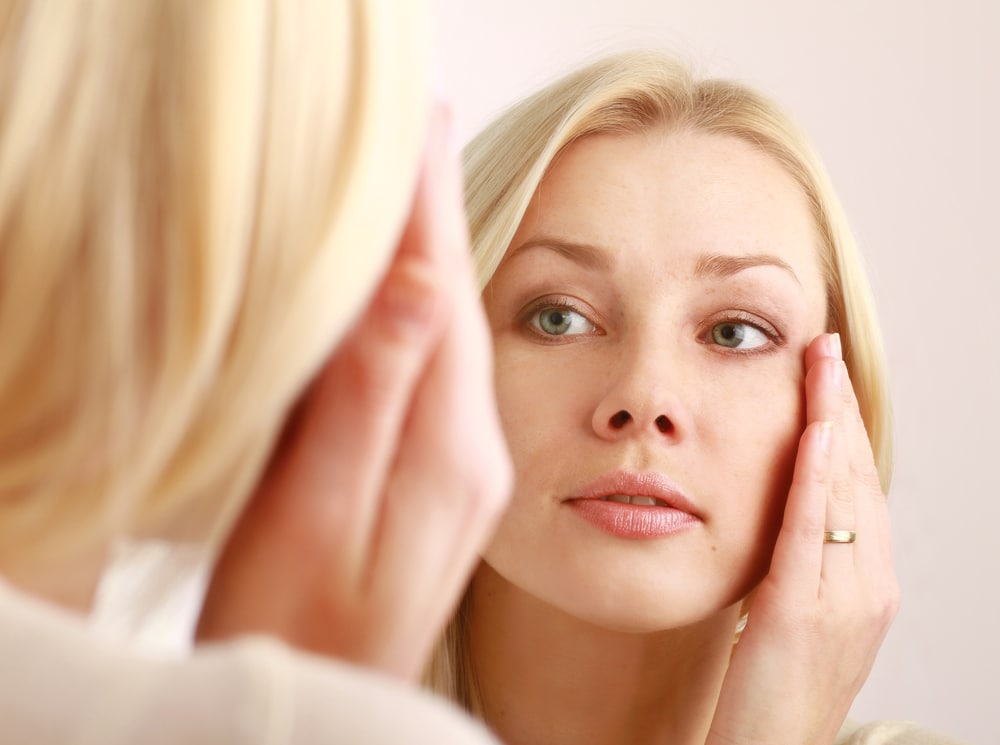 Woman looking closely at her skin in the mirror
